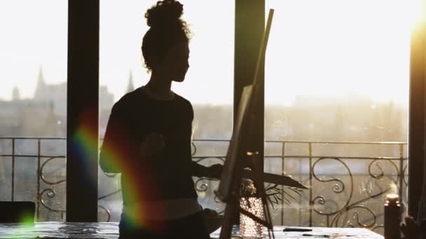 Unrecognizable figure of female artist drawing on easel in an art studio with panoramic windows. — Stock Video