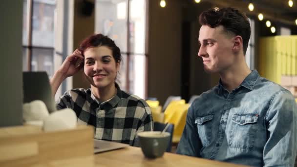 Junges Paar in stylischem Hipster-Urban-Outfit sitzt in einem offenen Co-Working-Raum und diskutiert etwas, während es auf den Laptop zeigt. — Stockvideo