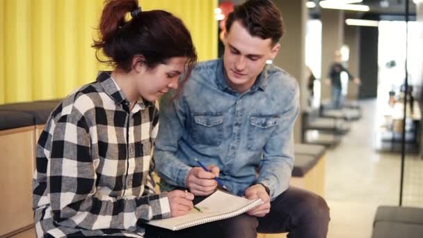 Dos jóvenes disfrutan de su tiempo juntos, dibujando algo en el bloc de notas. En interiores, imágenes en cámara lenta . — Vídeos de Stock