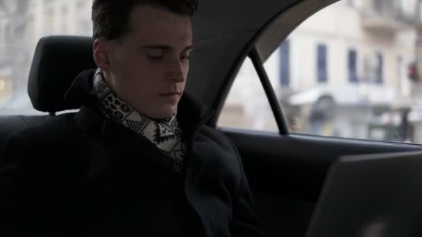 Atraente jovem macho está montando em um carro com laptop aberto em suas voltas . — Vídeo de Stock