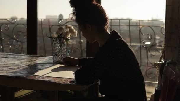 女画家坐在桌子上, 上面放着花, 用钢笔画在纸上, 在一个非常简约的艺术工作室的背景上。. — 图库视频影像