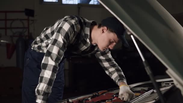 Bil service, reparation, underhåll och människor koncept - mekaniker man klädd arbete mantel och lock med handskar på händerna inspekterar alla mekanismer och deras funktion. — Stockvideo