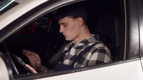 Serviço de reparação automóvel represanrarive usando tablet digital para analisar todos os principais indicadores do veículo que ele tem que reparar. Sentado dentro do carro . — Vídeo de Stock