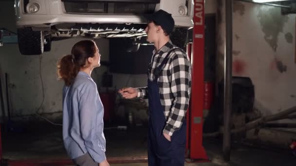 Εργαζόμενος βοηθάει θηλυκό πελάτη με όχημα και ελέγχει την τεχνική κατάσταση auto στην υπηρεσία αυτοκινήτων — Αρχείο Βίντεο