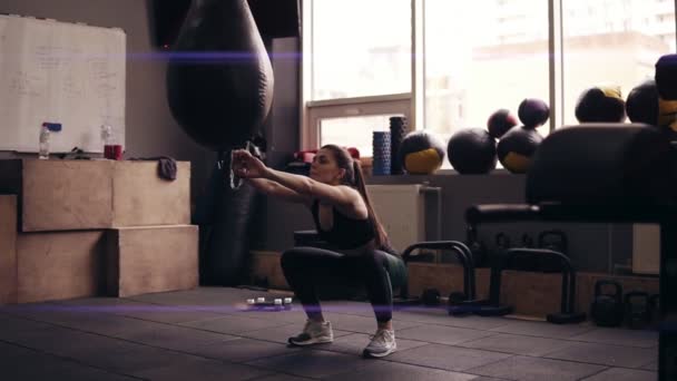 Молодая брюнетка со спортивным телом в черной спортивной одежде делает приседания в спортзале . — стоковое видео