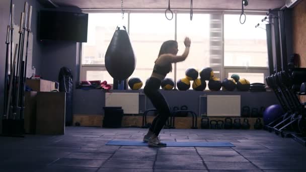 Filmación de una chica morena deportiva haciendo ejercicio en el gimnasio, saltando a la tabla en la alfombra del piso. Aptitud y asistencia sanitaria . — Vídeos de Stock