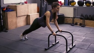 Çekici sportif esmer kız itme yapıyor ups spor salonunda push-up çubukları kullanarak. Güçlü kollar ve çekirdek üzerinde çalışıyor. Sağlıklı yaşam tarzı, fitness ve sağlık.