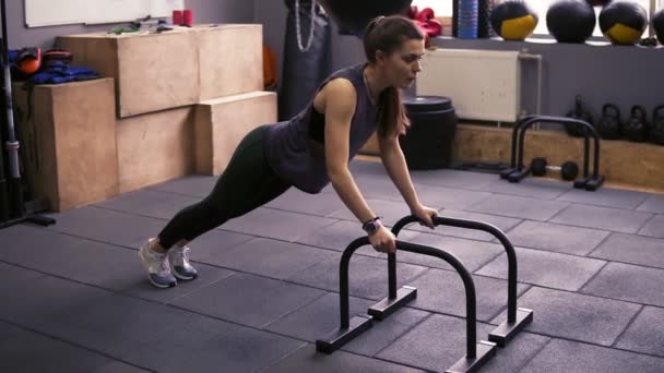 Çekici sportif esmer kız itme yapıyor ups spor salonunda push-up çubukları kullanarak. Güçlü kollar ve çekirdek üzerinde çalışıyor. Sağlıklı yaşam tarzı, fitness ve sağlık. — Stok video