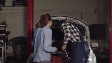 Şirin araba veya otomotiv teknisyeni iş bornoz ve şapkası giyen istemciden onu araç aynı zamanda seyir onun genç kadın, onun not defteri şikayetleri yazıyor.