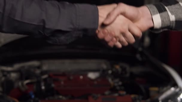 Primer plano plano de mecánico y cliente estrechando las manos en un taller de reparación de automóviles . — Vídeos de Stock