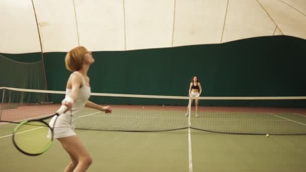 Zwei junge sportliche Frauen, die auf dem überdachten Platz Tennis spielen. Aktivität, gesunde Lebensweise — Stockvideo