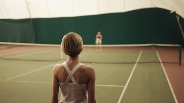 Rückseite Zeitlupenaufnahmen einer sportlichen Tennisspielerin, die auf dem Tennisplatz mit dem Schläger auf den Ball schlägt — Stockvideo
