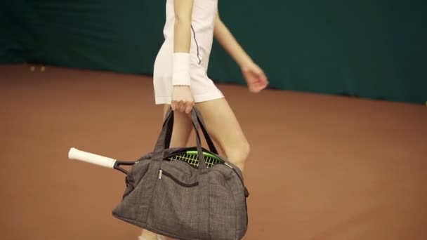 Vista de cerca de las piernas de la mujer joven en forma con una bolsa y raqueta de tenis y la preparación para el entrenamiento en la cancha — Vídeos de Stock