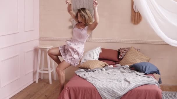 Menina loira sexy atraente em um vestido extravagante caindo na cama. Imagens internas — Vídeo de Stock