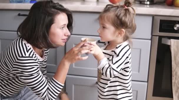 Moeder geeft haar dochter die een kopje water, klein meisje dranken, moeder lacht op de keuken — Stockvideo