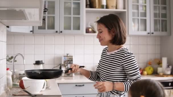 Vacker kvinna med kort brunt hår vänder över pannkakor i en stekpanna och leende — Stockvideo
