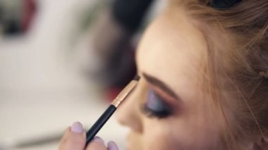 Stilist bazı kahverengi gölgeler bir fırça kullanarak ve dumanlı gözler ile güzel kadının sol kaş şekillendirme koyar. Hazırlık. Yan görünüm