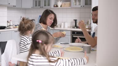 Güzel genç aile iki çocukla birlikte evde kahvaltı. Krep yemek ve dalga