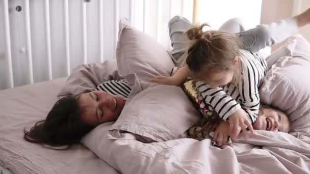 Счастливая мать играет вместе со своими двумя дочерьми в постели делая беспорядок в замедленной съемке — стоковое видео