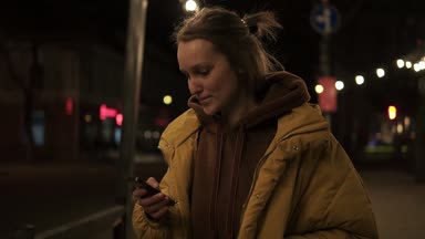 Kısa saçlı kız akşam şehir gülümseyen, durur ve manifatura smartphone içinde size yürür. El görüntüleri