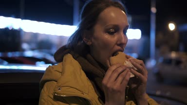 Sparkles yüzünde ile aç genç kadın dışında bir hamburger yiyor. Memnun. Yan görünüm