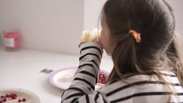 Ein kleines Mädchen sitzt auf einem Stuhl und isst im gestreiften Hemd dünne Pfannkuchen — Stockvideo