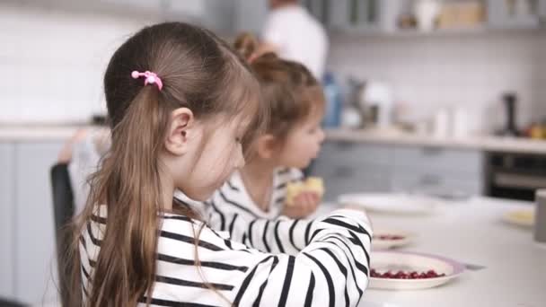 Dos hermanitas comen panqueques en la mesa con su padre detrás. Vista lateral — Vídeo de stock