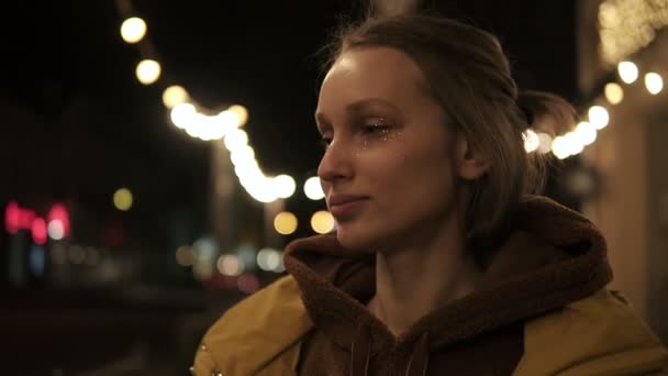 Красивая молодая женщина на улице в жёлтом пальто поворачивается к камере, курясь и блестит блестками. Свет позади — стоковое видео