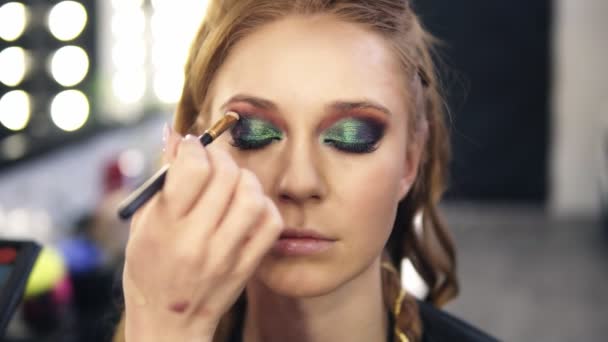 Visage meester maakt laatste hand voor ogen make-up voor een mooi model met kameleon ogen make-up effect. Vooraanzicht — Stockvideo