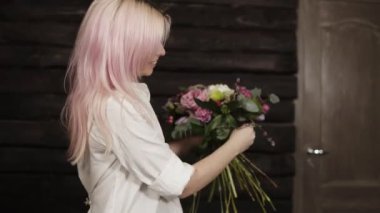 Pembe saçlı genç bir kadın kompozisyon söğüt dalları ile tamamlayan buket tasarımı yapar. Gülümseyerek. Koyu arka plan