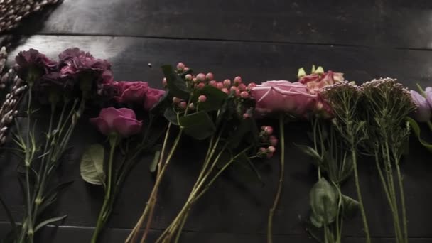Medium close up metraje de una colorida variedad de flores en flor expuestas en una fila en una superficie de madera oscura — Vídeos de Stock