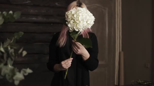 Rosa haarige schöne Floristin mit riesigen weißen Hortensienblüten in den Händen. nimmt Extrablätter ab — Stockvideo