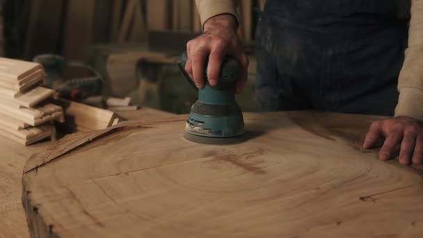 Mens, αγενής, που εργάζονται τα χέρια του carpenter χειρίζονται το ξύλο με μια μηχανή λείανσης. Ελέγχει την ομαλή επιφάνεια με το χέρι — Αρχείο Βίντεο