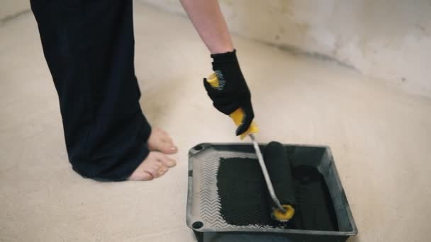 La chica de la pared de pintura con rodillo en la habitación con una pintura negra que se encuentra frente a esa pared. Movimiento lento — Vídeos de Stock