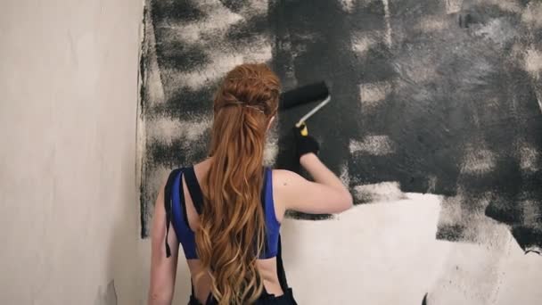 Krásná žena v tmavé celkově maluje zdi pokoje s pomocí. Pohled zezadu — Stock video