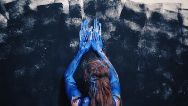 Chica atractiva, caliente en un traje de baño azul untado con pintura azul y dibuja en la pared. Vista lateral trasera — Vídeos de Stock