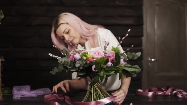 Florista profesional chica ata la parte inferior del ramo con cintas de seda rosa. Estudio oscuro. Movimiento lento — Vídeo de stock