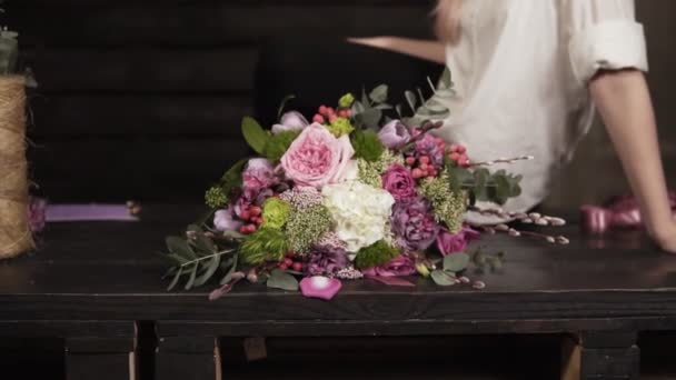 Úchvatné zpomalené záběry krásné jemné mladé ženy. Ona sedí na stole s nádhernou kytici vedle ní. Házení hrst lístků do fotoaparátu — Stock video