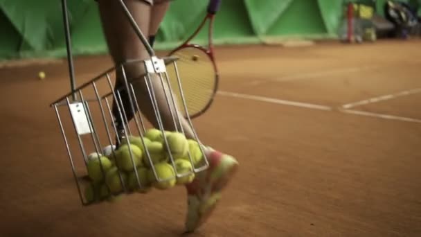 Aiming footage of a disabled womans legs. Slender girl collects balls with a tennis basket. Indoors tennis court — Stock Video