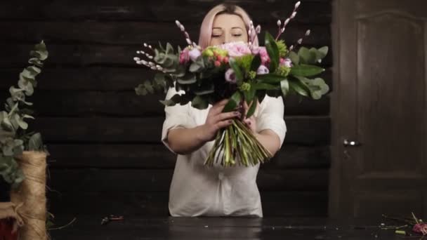 Charming girl florist presents her work, puts on the table a beautiful bouquet of colorful flowers on long stable stems. Pretty smiling, gesturing with hands. Front view — Stock Video