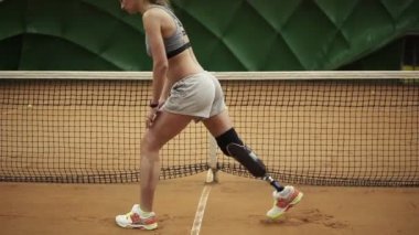 Bir kadınla bir protez bacakları, lunges Tenis Kortu arka planı yapma uzanır. Spor giyim. Ağır çekim