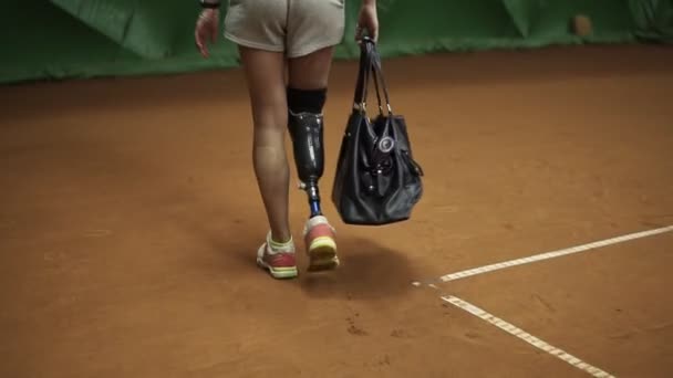 跟踪一个无效的运动员在网球场上走在她的袋子球拍的镜头。后退视图。慢动作 — 图库视频影像