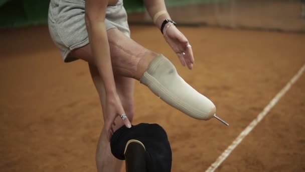 Injured beautiful brave woman athlete puts the prosthesis on the right leg standing on the tennis court. Close up — Stock Video