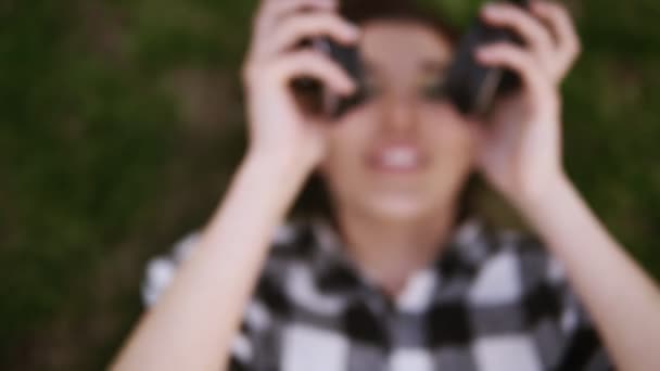 Casques dans les mains des femmes. Charmante fille couchée sur le dos sur l'herbe, mettre des écouteurs et écouter avec plaisir de la musique. Tirer depuis le haut 