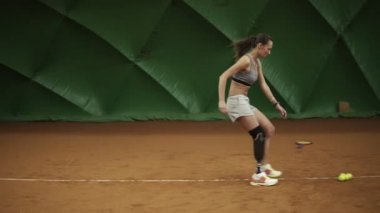 Tenis topları köşelerde ayarlama mahkeme çevresinde atlet bacak protezi üzerinde çalışır. Eğitimler. Spor giyim. Kapalı