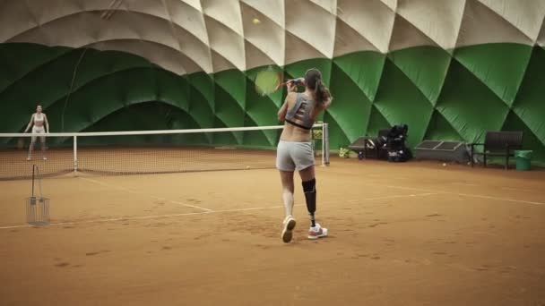 Two beautiful, tall girls in sports clothes and bras are playing tennis. Indoors. Moving camera — Stock Video