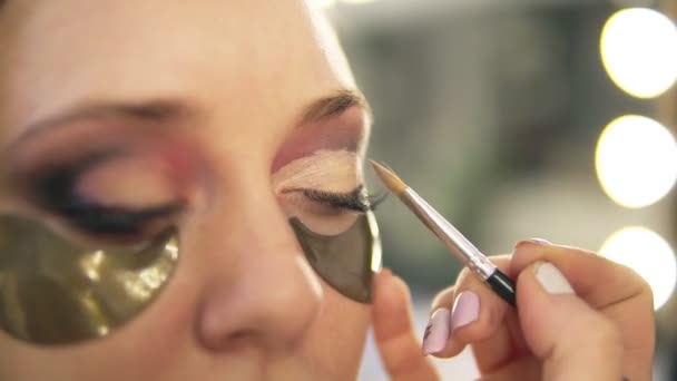 Make-up artist att sätta på ljusa ögon skuggor på modeller öga. Närbild. Patchar. Sidovy — Stockvideo
