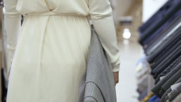 Seguimiento de imágenes de una hermosa mujer en blanco, caminando por la tienda de tela con un rollo de textil ligero en la mano derecha. Primer plano disparado desde atrás — Vídeos de Stock