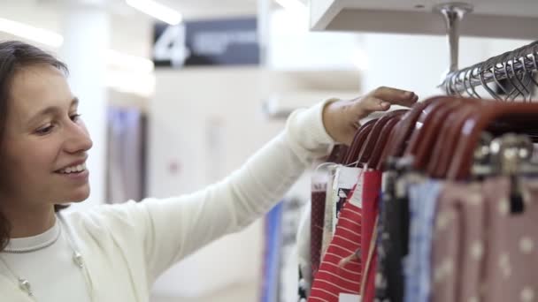 The girl is enthralled with different samples of color printed fabrics on the hangers and chooses one variant. Textile store. Side view — Stock Video