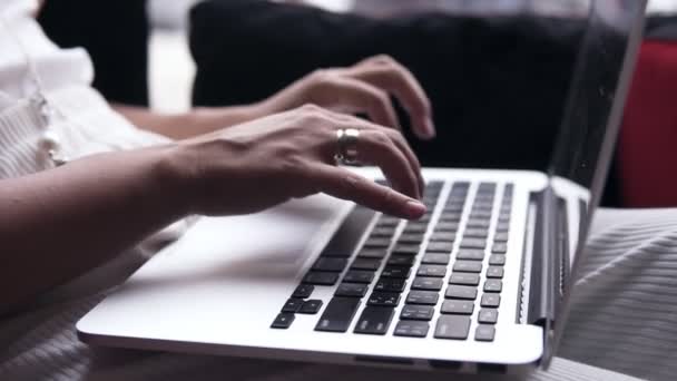 Apunta imágenes de una joven mujer escribiendo con las manos en un portátil de plata. La computadora está en sus piernas. Pantalla negra — Vídeo de stock